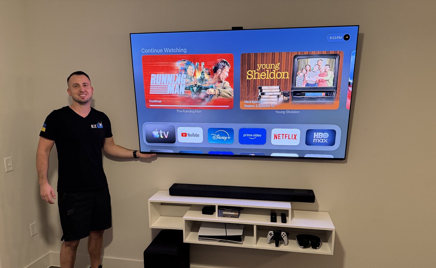 Andriy owner of EZ TV Mounting standing next to large TV soundbar and floating shelf installation in Dallas TX