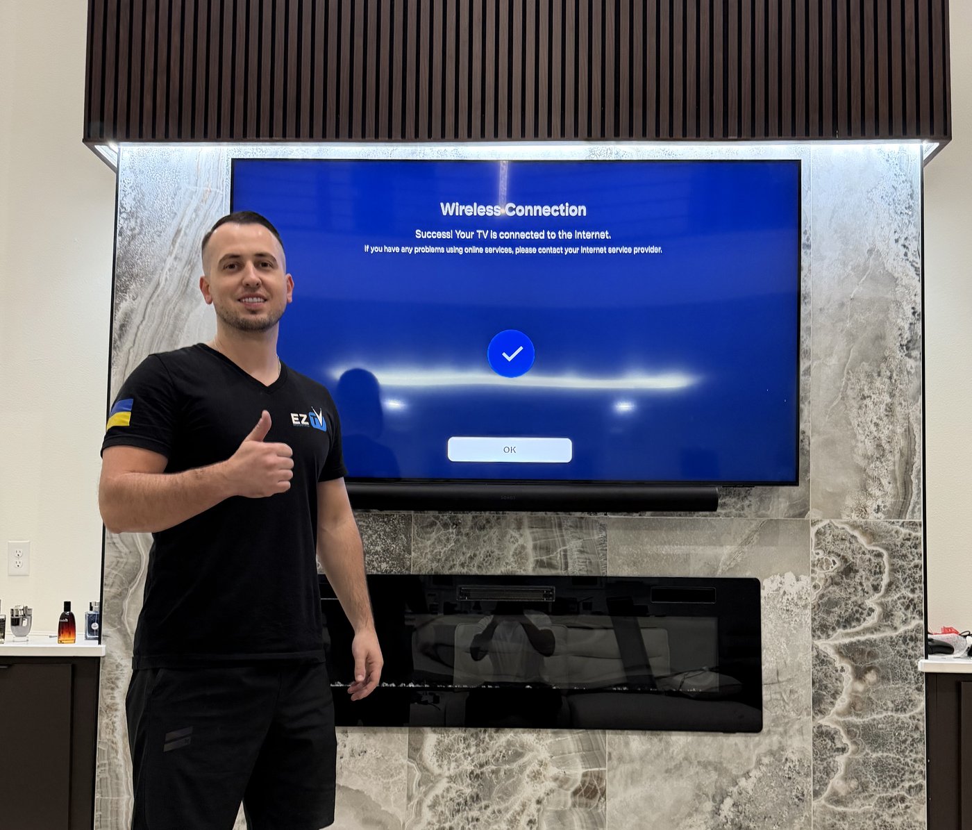 Andriy from EZ TV Mounting giving thumbs up next to completed marble fireplace TV installation in Dallas TX